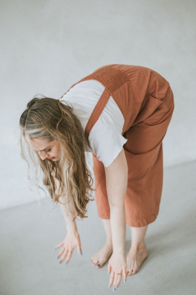 Yoga teacher in a terracotta jumpsuit performing a halfway lift